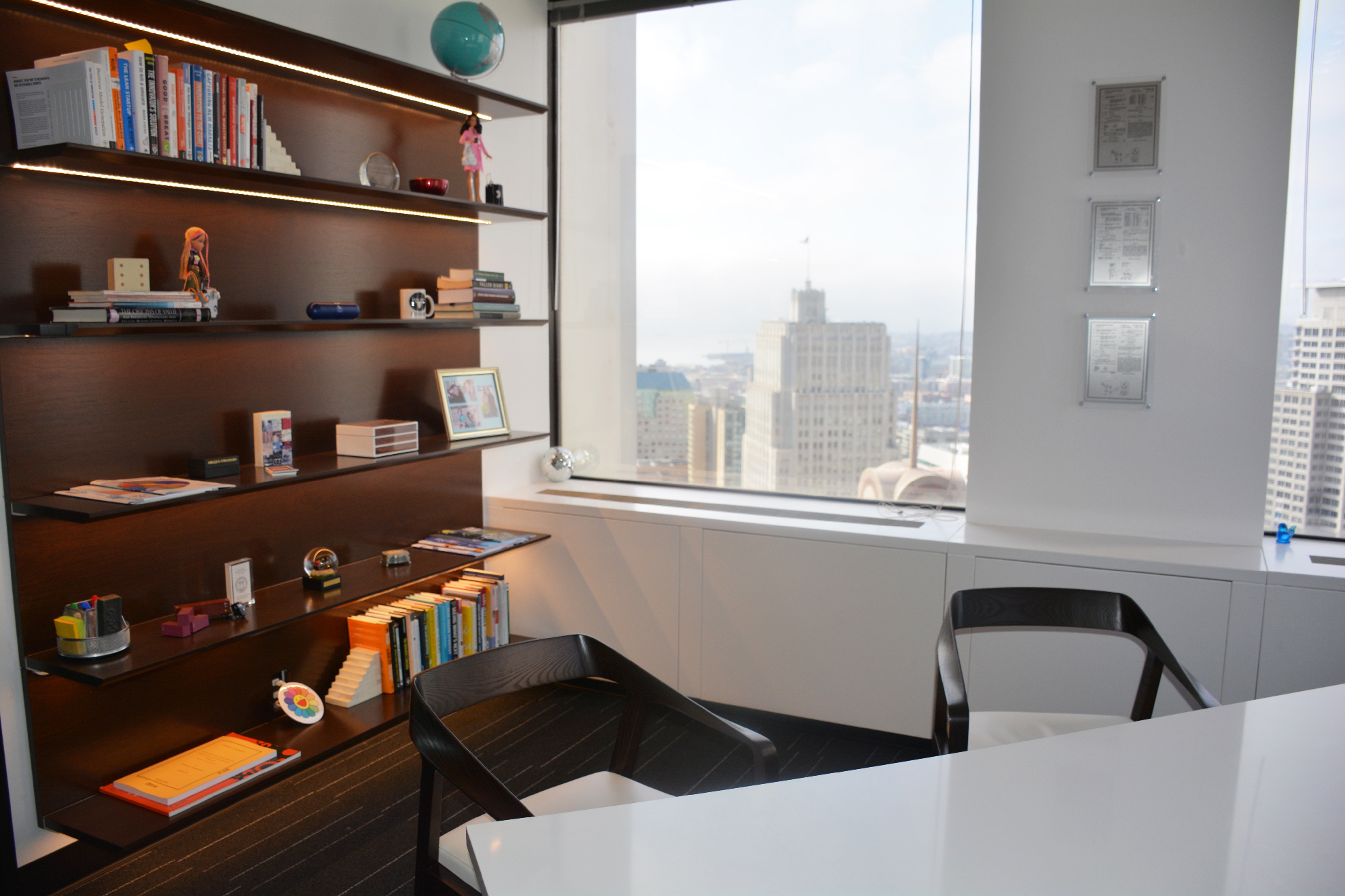 Gorgeous minimal office with designed chairs and custom lit shelving.