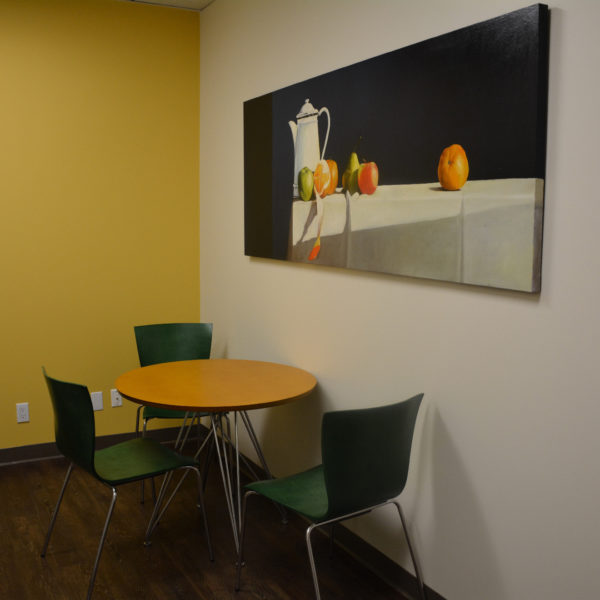 This is a pleasant eating space with a table and 3 chairs designed with the orange and green of art in mind.